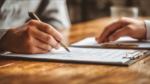 Person signing a document on a clipboard with a pen during a business meeting