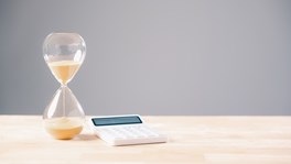 Hourglass beside calculator and coins illustrating business cashflow pressure and late payment deadlines