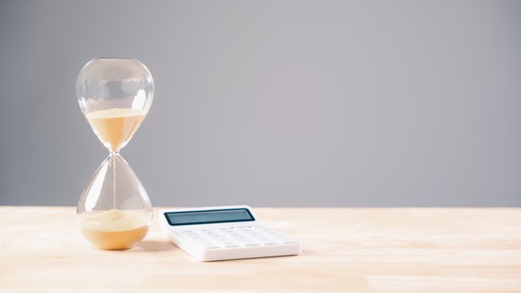 Hourglass beside calculator and coins illustrating business cashflow pressure and late payment deadlines